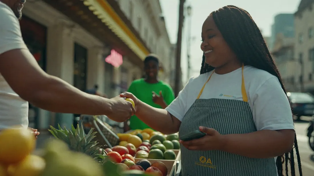 A market trader handing fruit to a smiling customer